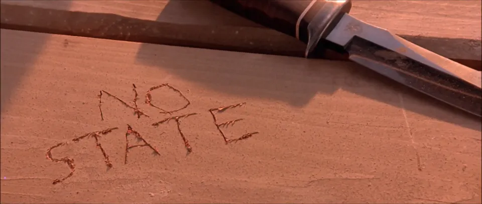 The phrase "No State" carved into a wooden table